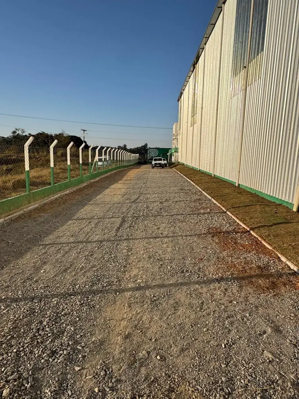 Base de brita compactada pronta para receber a imprimação, ao lado de galpão industrial