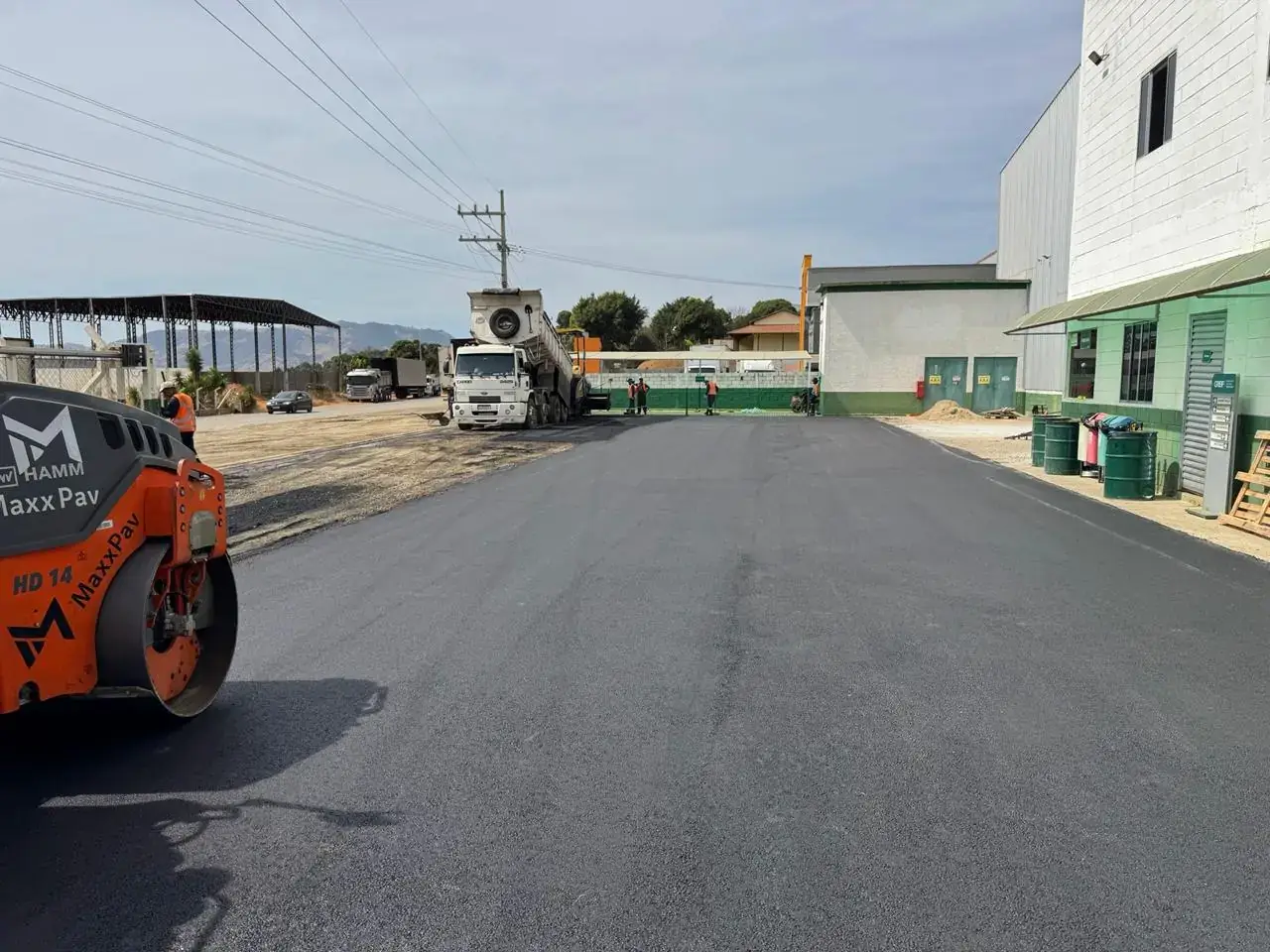 Pavimento asfáltico concluído em pátio industrial, com rolo compactador em primeiro plano