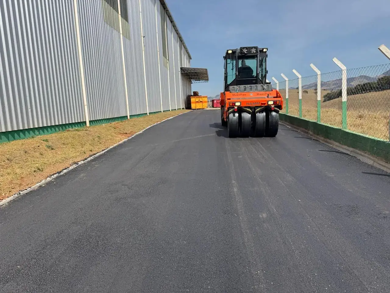 Rolo de pneus compactando a capa de CBUQ recém-aplicada em via interna de galpão