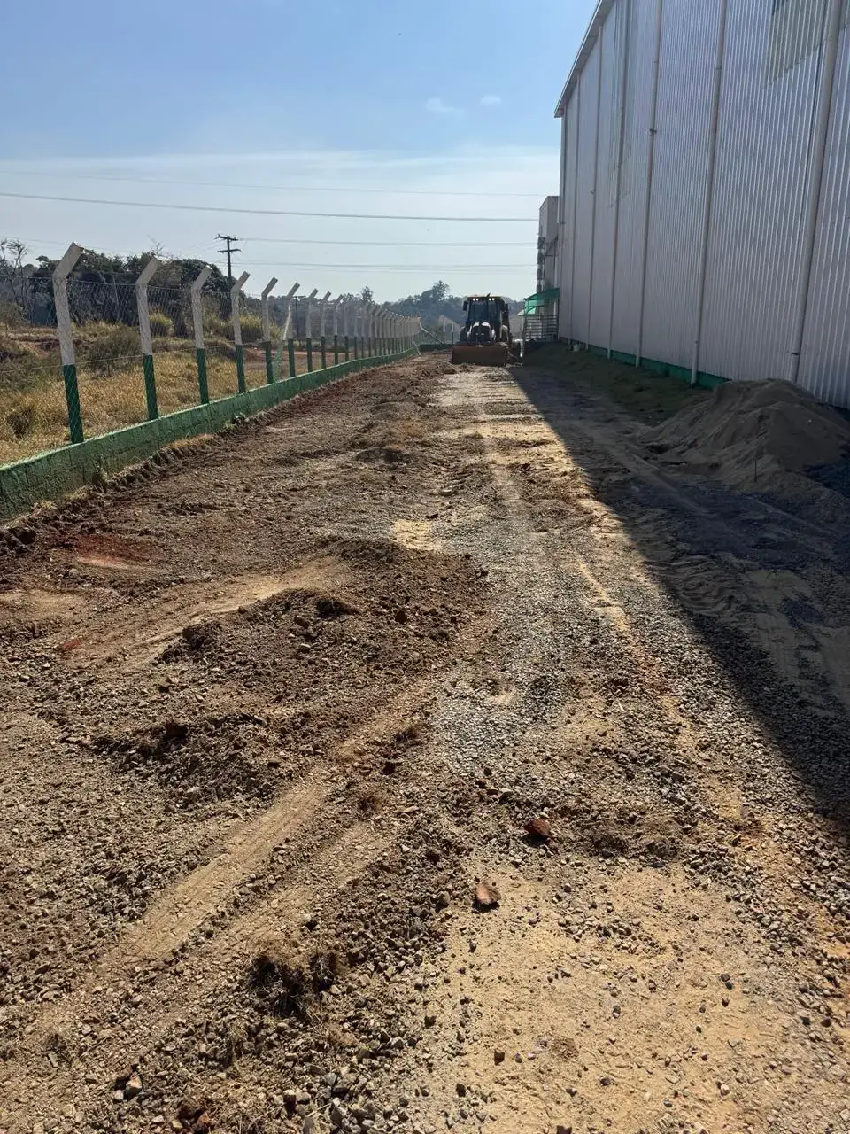Terreno de terra regularizado ao lado de um galpão, antes da pavimentação asfáltica