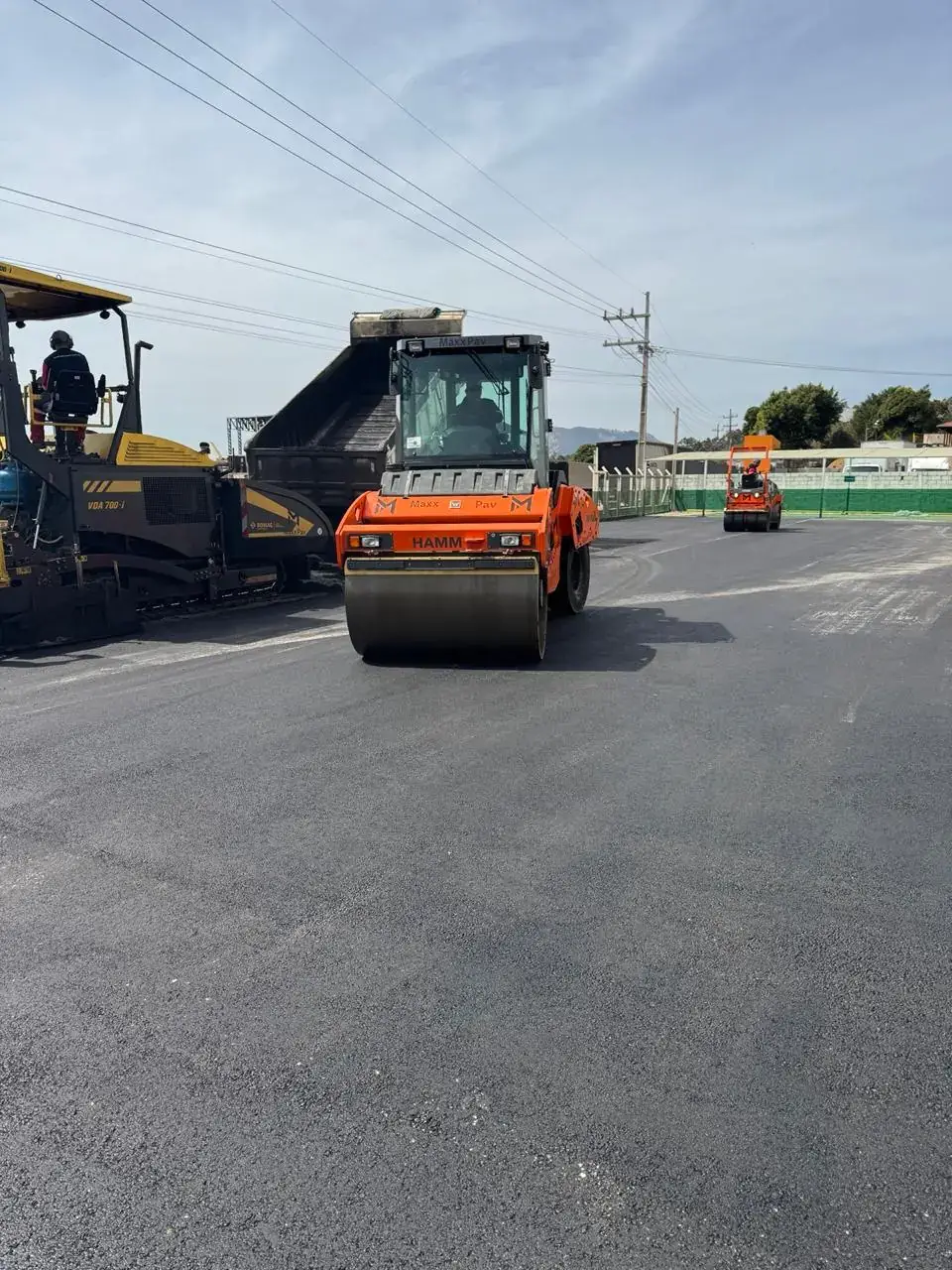 Vibroacabadora, caminhão de massa e rolo compactador aplicando CBUQ em pátio industrial