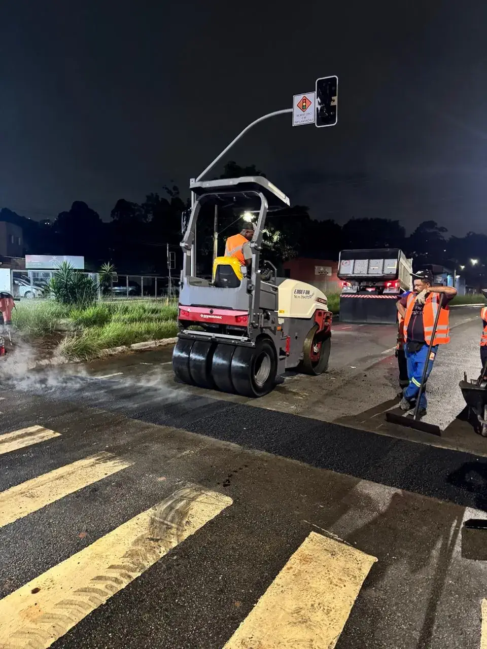 Rolo compactando a capa nova de um recapeamento noturno em via urbana